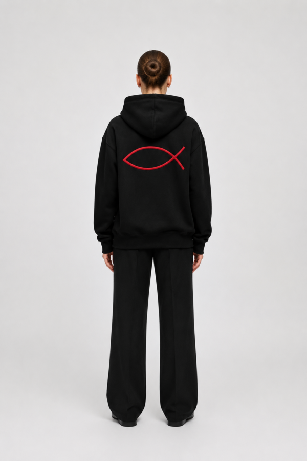 Ein Mensch trägt eine schwarze Kapuzenjacke mit rotem Fischsymbol, symbolisch für Christentum.